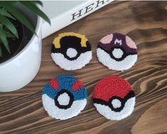 four crocheted pokemon coasters sitting on top of a wooden table next to a potted plant