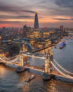 an aerial view of the tower bridge in london, england at sunset with boats on the river below