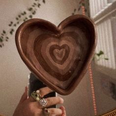 a wooden heart shaped dish being held by a woman's hand in front of a mirror