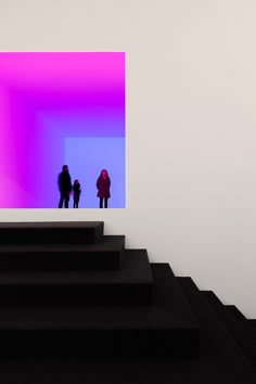 three people are standing in front of a purple and blue square on a white wall