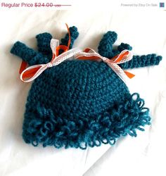 a crocheted blue hat with an orange ribbon on the top and white background