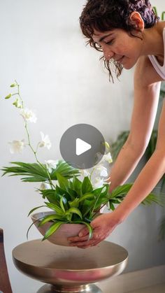 a woman placing flowers in a pot on top of a metal stand with a planter