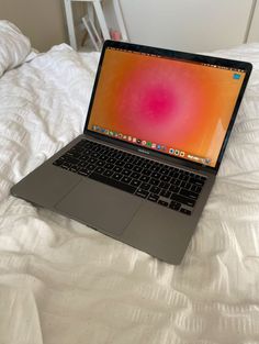 an open laptop computer sitting on top of a white bed covered in blankets and pillows