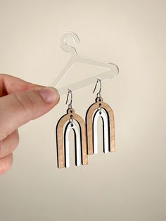 a pair of wooden earrings hanging from a hanger on a white wall with a hand holding it