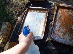 a person is holding a spray bottle in front of two rusty pans on the ground