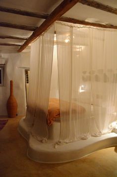 a white bed with sheer curtains on top of it in a room filled with furniture