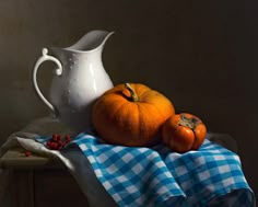 two pumpkins and a white pitcher on a table