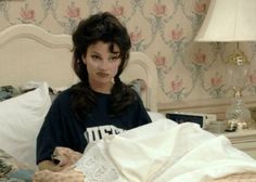 a woman sitting on top of a bed next to a white comforter and lamp