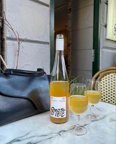 two wine glasses and a bottle sitting on a table with a handbag next to it