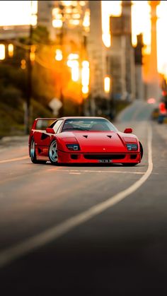 a red sports car is driving down the street in front of tall buildings at sunset