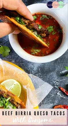 someone holding a taco in their hand over a bowl of soup with limes and cilantro on the side