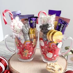 two mugs filled with candy and candies on a wooden table next to christmas decorations