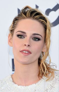 a woman with blonde hair and blue eyeshadow, wearing a white top is looking at the camera