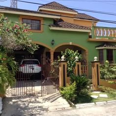 a car is parked in front of a green house with flowers on the balcony and balconies