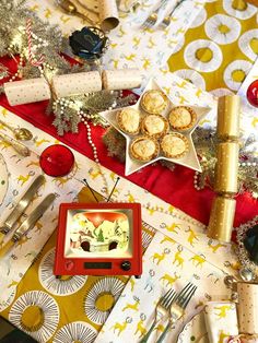 a table topped with plates and silverware next to christmas decorations on top of a red table cloth