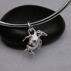 a silver necklace with a bird on it sitting on a black rock next to a stone