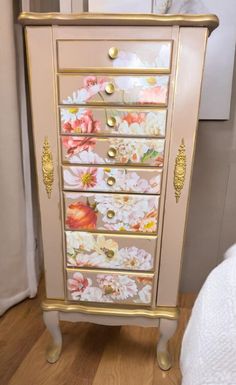 a pink and gold dresser with flowers painted on the drawers, sitting in a room next to a bed