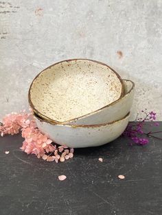 two white bowls sitting on top of a table next to some pink flowers and petals