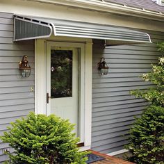 the front door of a gray house with white trim and an awning over it