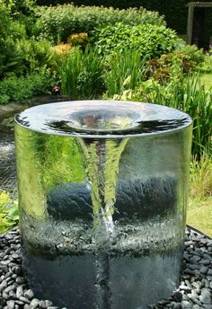 a water fountain in the middle of a garden with rocks and gravel around it, surrounded by greenery