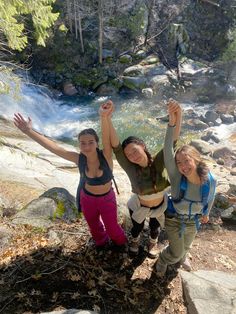 three young women standing on the side of a river with their arms in the air