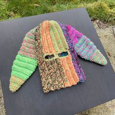 two knitted scarves sitting on top of a piece of black paper in the grass