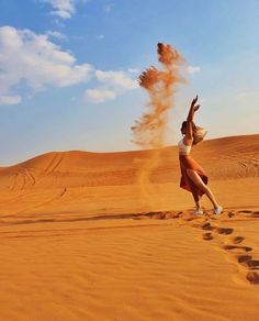 a woman standing on top of a sandy beach next to a red object in the air