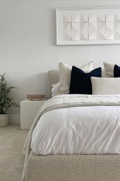 a bed with white sheets and pillows in a bedroom next to a potted plant