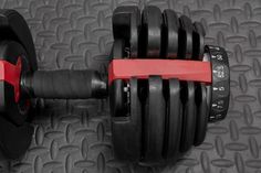 a pair of dumbbells with red handles sit on a black mated surface