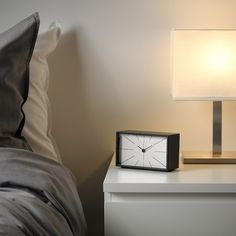 a clock sitting on top of a white nightstand next to a night stand with a lamp