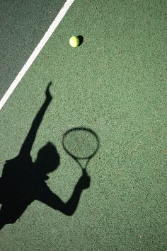 a shadow of a person holding a tennis racquet on a tennis court with a ball in the air