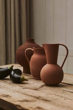 three vases sitting on top of a wooden table next to two black eggplant