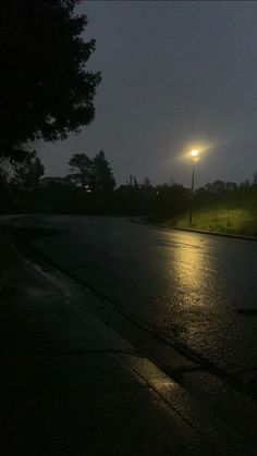 an empty street at night with the moon in the sky and trees on the side