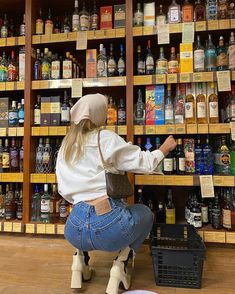 a woman sitting on a stool in front of a shelf full of liquor bottles