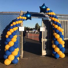 blue and yellow balloons are attached to the gate at an outdoor tennis court with stars on them