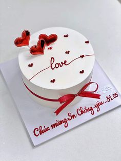 a white cake with red hearts on it and the words love is written in cursive writing