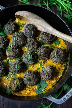 a pan filled with meatballs covered in sauce and parsley next to a wooden spoon