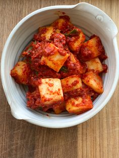 a bowl filled with tofu and sauce on top of a wooden table next to a fork