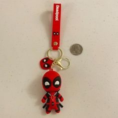 a red keychain with a deadpool character on it and a coin sitting next to it