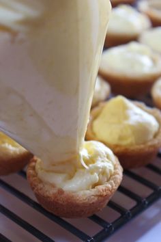 a person is spreading icing onto some cupcakes on a cooling rack with other muffins in the background