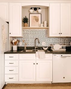 a kitchen with white cabinets and black counter tops is pictured in this image, there are dishes on the shelf above the dishwasher