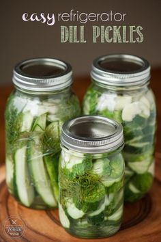 three mason jars filled with cucumbers and dill pickles on a wooden tray