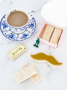 a cup of coffee next to some cut out cookies and a box of crackers