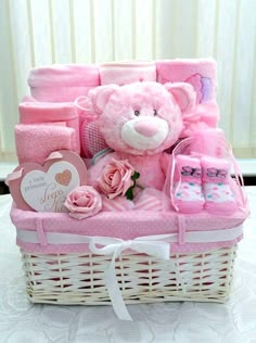 a pink teddy bear sitting in a basket filled with baby items on top of a table