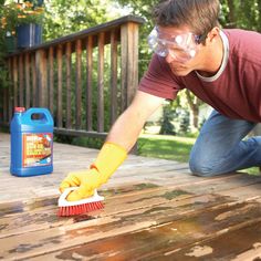 a man in safety goggles and yellow gloves cleaning a wooden deck with a brush