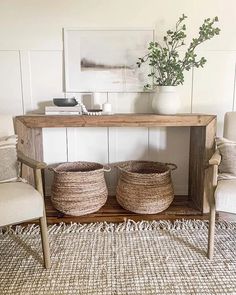 two baskets sitting on top of a wooden table next to a white vase and chair