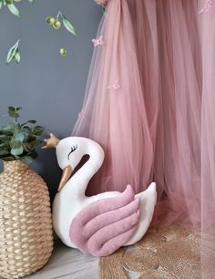 a stuffed swan sitting on the floor next to a potted plant and pink tulle curtains