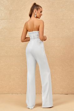 a woman wearing white pants and a strapless top standing in front of a wall