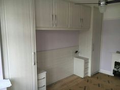 an empty room with white cupboards and drawers on the wall, in front of a fireplace