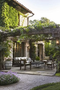 an outdoor patio with chairs and tables surrounded by greenery on either side of the house